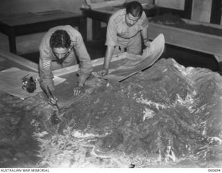ST. LUCIA, QLD. 1943-11-24. V281550 SERGEANT M. R. ANGUS (LEFT) AND SX21098 LIEUTENANT J. E. MAHER OF GENERAL STAFF INTELLIGENCE, ADVANCED LAND HEADQUARERS, WORKING ON A MODEL OF THE NEW GUINEA ..