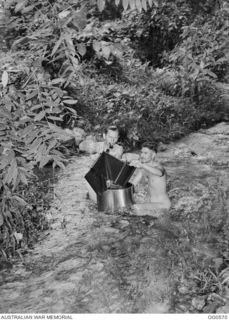 MILNE BAY, PAPUA. 1943-07-31. NAKED MEN, LEADING AIRCRAFTMAN (LAC) H. HARDIE, KOGARAH, NSW (LEFT) AND LAC K. W. GILL, SYDNEY, NSW, WASHING A FILM IN A JUNGLE STREAM AFTER IT WAS DEVELOPED IN TOTAL ..