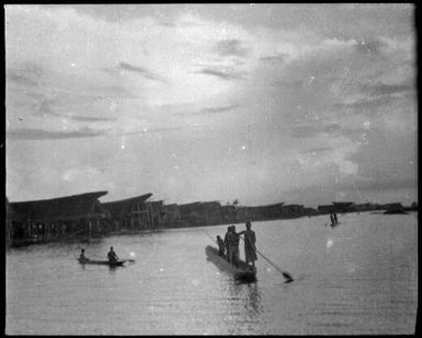 Three canoes with standing paddlers and a village beyond, Kambaramba Lake, Sepik River, New Guinea, 1935 / Sarah Chinnery