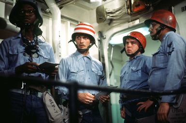 Members of a firefighting team wearing protective helmets, and a member of a repair party, equipped with a sound-powered phone, left, listen to instructions before taking part in a drill aboard the amphibous assault ship USS GUAM (LPH 9)