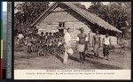 Man speaks with the village chief in front of the school and chapel, Papua New Guinea, ca.1900-1930