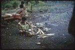 Food preparation: Kitemwalusa peels yams for cooking, girl in red skirt behind her