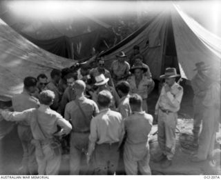 HOLLANDIA, DUTCH NEW GUINEA. C. 1944-06. WING COMMANDER W. D. BROOKES (RIGHT), MINISTER FOR AIR, ARTHUR DRAKEFORD (IN HAT), AND MINISTER FOR WAR ORGANISATION OF INDUSTRY, JOHN DEDMAN TALKING TO ..