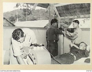 LAE, NEW GUINEA. 1944-11-09. CORPORAL W. TAYLOR (3) AND SERGEANT D. COOPER (1), PHYSIOTHERAPISTS OF THE 112TH CONVALESCENT DEPOT GIVING WRIST AND LEG EXERCISES TO SAPPER C.B. BLUNDEN, 2/2ND DOCKS ..