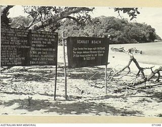 SCARLET BEACH, FINSCHHAFEN AREA, NEW GUINEA. 1944-03-13. THE SIGN TO THE RIGHT MARKS THE POINT OF THE ATTEMPTED JAPANESE INVASION. TWO WRECKED JAPANESE BARGES LIE IN THE BACKGROUND. THE BARGES IN ..