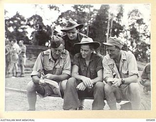 JACQUINOT BAY, NEW BRITAIN, 1945-08-23. AUSTRALIAN AND NEW ZEALAND PERSONNEL STUDYING THE PROGRAMME AT THE VICTORY CUP RACE MEETING HELD ON THE AIRSTRIP USING WOODEN HORSES CONTROLLED BY THE THROW ..