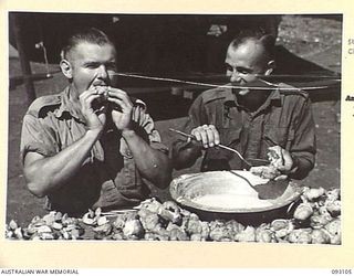 WEWAK AREA, NEW GUINEA, 1945-06-13. PTE C.J. JONES, 2/2 INFANTRY BATTALION (1), SAMPLING A CREAM PUFF, WHILE SAPPER L.R. POLLARD, 2/3 FIELD COMPANY (2), FILLS PUFFS WITH ARTIFICIAL CREAM. THE MAIN ..