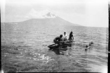 Three people on an outrigger canoe with Manam Island in the background, Awar, Sepik River, New Guinea, 1935 / Sarah Chinnery