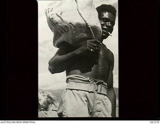 Dumpu, New Guinea. 1943-12-19. A native carrying a bag of Christmas parcels for the soldiers, which has just been unloaded from an aircraft at the Dumpu airstrip in the Ramu Valley area