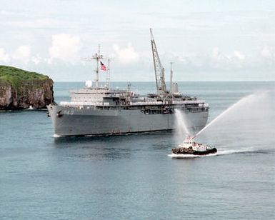 A port bow view of the submarine tender USS FRANK CABLE (AS 40), entering Apra Harbor, Guam. A tugboat renders a salute from its water cannons. (Substandard image)