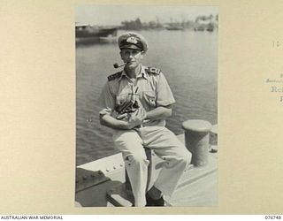 LANGEMAK BAY, NEW GUINEA. 1944-10-23. LIEUTENANT N.K. WALLIS, COMMANDING THE RAN CORVETTE, GYMPIE, NURSING THE SHIP'S MASCOT