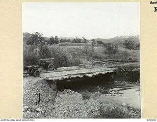 WAU - LAE ROAD, NEW GUINEA, 1944-02-26. TWENTY FIVE MILES FROM WAU A NEW BRIDGE BEING CONSTRUCTED ACROSS THE BAIME CREEK A FEW HUNDRED YARDS FROM THE WATUT RIVER. SPANNING 32 FEET IT CONSISTS OF ..