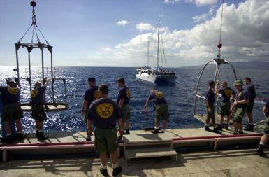 US Navy (USN) divers assigned to Mobile Diving Salvage Unit One (MDSU-1), prepare the diving stages on the deck of the Crowley Marine 450-10 Barge, during recovery of the sunken Japanese fishing vessel, Ehime Maru. A chartered vessel is visible in the background