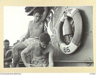 ALEXISHAFEN, NEW GUINEA. 1944-04-30. B3054 ABLE SEAMAN H. KERNOVSKE (2), COILS A ROPE ABOARD HMA MOTOR LAUNCH 816 WATCHED BY ABLE SEAMAN MORETON (1), WHO IS SITTING ON FLOATS ALONGSIDE THE ..