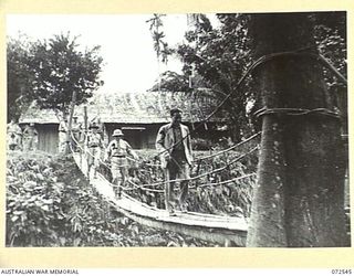 MILNE BAY, NEW GUINEA. 1944-04-20. THE HONOURABLE E.J. WARD, MINISTER FOR EXTERNAL TERRITORIES IN THE AUSTRALIAN GOVERNMENT (3), WITH MEMBERS OF HIS OFFICIAL PARTY CROSSING A SUSPENSION BRIDGE FROM ..