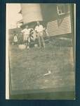 Burt Waldy and Chuck[?] standing next to water tank beside house, with Biamen walking away from house in background, [Bulolo?], New Guinea, c1932 to 1933