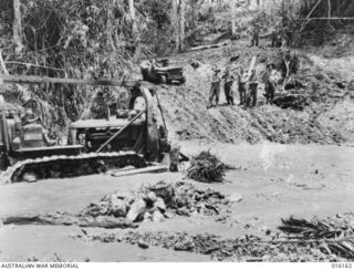 FINSCHHAFEN AREA, NEW GUINEA. 19 NOVEMBER 1943. A BULLDOZER BUILDS UP A CROSSING IN THE QUOJA RIVER ON THE MAIN TRACK TO THE FORWARD AREAS FROM FINSCHHAFEN. THE CROSSING HAD BEEN WASHED AWAY BY ..