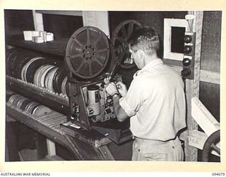 YALU, NEW GUINEA. 1945-08-03. PRIVATE L.H. SPIELVOYEL, NEW GUINEA TRAINING SCHOOL, OPERATING THE PROJECTOR IN THE BIO BOX