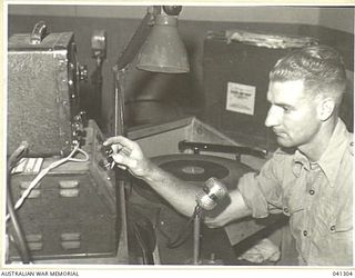 LAE, NEW GUINEA. 1945-09. ANNOUNCER OF LAE RADIO STATION, (9.AB) OPERATING AMPLIFIER FOR TURN TABLE AND MICROPHONE OF THE SET ORIGINALLY BUILT OF JUNK, MAINLY JAPANESE, BUT WITH SOME AUSTRALIAN AND ..