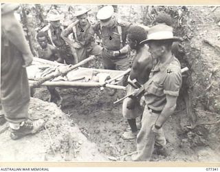 TOROKINA AREA, BOUGAINVILLE ISLAND. 1944-11-30. TX2002 BRIGADIER J. FIELLD, DSO, ED, COMMANDING, 7TH INFANTRY BRIGADE (3) WATCHING NATIVE BOYS CARRYING WOUNDED JAPANESE PRISONERS BACK TO THE ..
