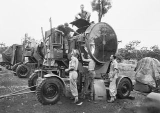 Port Moresby, New Guinea. 1944-05-30. Members of the Moresby Fortress Workshop overhauling searchlight equipment. Left to right: Back: Sergeant A. Callaghan, and Lance Sergeant T. A. Brazil. Front ..