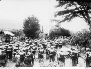 PAPUA. 1942-11-14. ALLIES RETAKE KOKODA. AUSTRALIAN FLAG IS RAISED AS TROOPS ENTER KOKODA, WATCHED BY A GROUP OF AUSTRALIAN TROOPS