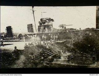 Rabaul (?), New Britain. c.1915. The RAN destroyer HMAS Warrego docked at a wharf with RAN members of the Australian Naval and Military Expeditionary Force (AN&MEF) sitting on the wharf's steps ..