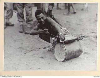 BERRY'S HILL, CENTRAL BOUGAINVILLE, 1945-06-27. A NATIVE CARRIER TYING TWO 4.2 INCH MORTAR BOMBS TO A TIN OF TEA DURING THE MOVEMENT OF SUPPLIES TO 7 INFANTRY BATTALION TROOPS ALONG THE NUMA NUMA ..