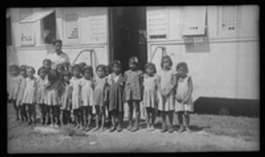 [Woman and group of children outside building]