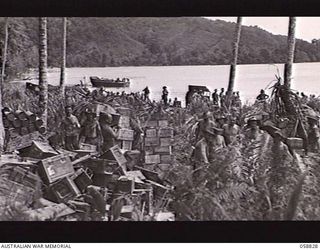 LANGEMAK BAY, NEW GUINEA, 1943-10-20. THE BEACHHEAD WHERE THE 2/24TH AUSTRALIAN INFANTRY BATTALION EMBARKED ON LANDING CRAFT FOR LAUNCH JETTY. NOTE THE BOXES OF STORES STACKED IN THE FOREGROUND