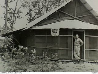 TOROKINA, BOUGAINVILLE ISLAND, SOLOMON ISLANDS. 1945-08-25. "DOZER INN" IS THE NAME GIVEN TO THE OFFICERS MESS OF NO. 7 AIRFIELD CONSTRUCTION SQUADRON RAAF (ACS). STANDING IN THE DOORWAY IS THE ..