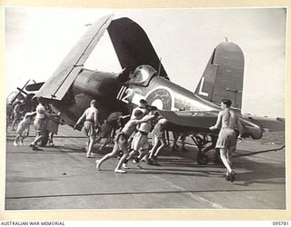 AT SEA OFF RABAUL, NEW BRITAIN. 1945-09-06. A CORSAIR AIRCRAFT BEING MAN-HANDLED ON THE FLIGHT DECK OF THE AIRCRAFT CARRIER HMS GLORY DURING PREPARATIONS FOR TAKEOFF. CORSAIRS WILL CIRCLE OVERHEAD ..