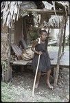 Mortuary ceremony: Bomtavau with basket of banana leaf bundles behind her on house veranda