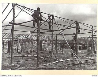 CAPE WOM, NEW GUINEA, 1945-05-29. NATIVES WORKING ON LARGE STORE HUTS AT THE FIELD MAINTENANCE CENTRE. IN THE BACKGROUND ARE COMPLETED HUTS FILLED WITH STORES
