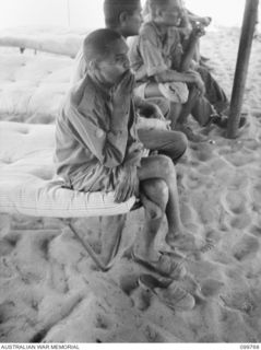 BORAM BEACH, NEW GUINEA, 1945-10-14. ELEVEN INDIAN SOLDIERS WERE LIBERATED FROM THE JAPANESE AT MARIENBERG IN THE SEPIK RIVER AREA. SHOWN, AN INDIAN WARRANT OFFICER 2 AWAITING ATTENTION BY MEDICAL ..