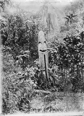 Unidentified men alongside a carved wooden statue in bush, Vanuatu