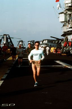 Crewmen and Marines run on the flight deck of the amphibious assault ship USS GUAM (LPH-9) during morning physical training (PT)