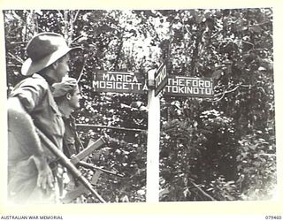 BOUGAINVILLE ISLAND. 1945-03-08. NX91097 LANCE CORPORAL E.R. JOHNSON (1) AND NX133745 L. CPL N.T. HALPIN (2), 25TH INFANTRY BATTALION INSPECTING A NEWLY ERECTED ROAD SIGN AT THE BARARA ROAD ..