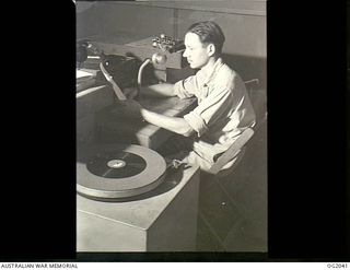 MADANG, NEW GUINEA. C. 1944. 435397 SERGEANT F. E. J. SHEPPARD OF BRISBANE, QLD, FORMER ABC ANNOUNCER, IS CHIEF ANNOUNCER FOR RAAF RADIO. HE IS IN FRONT OF THE MICROPHONE WITH HIS SCRIPT IN THE ..