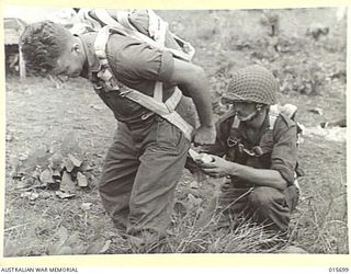 1943-09-15. PARATROOPS LAND AT NAZAB. AN AUSTRALIAN, GUNNER ANDERSON, ASSISTS GUNNER GRIBBEN, ANOTHER AUSTRALIAN, TO PUT ON HIS PARACHUTE BEFORE THEY AND OTHER AIRBORNE AUSTRALIAN ARTILLERYMEN ..