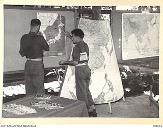 YALU, NEW GUINEA. 1945-08-03. LIEUTENANT R.E. PYM (1) AND LIEUTENANT H.J. JESSON (2), ARRANGING WALL MAPS AT THE NEW GUINEA TRAINING SCHOOL