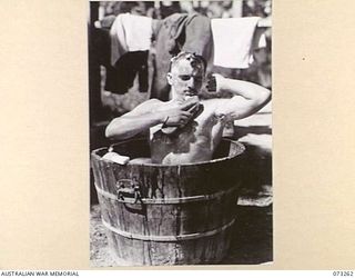 ALEXISHAFEN, NEW GUINEA. 1944-05-16. VX26926 LANCE CORPORAL J REYNOLDS (1), A MEMBER OF THE 2/15TH FIELD AMBULANCE, MAKING USE OF AN ABANDONED JAPANESE TUB AT THE OLD CATHOLIC MISSION, THE PRESENT ..