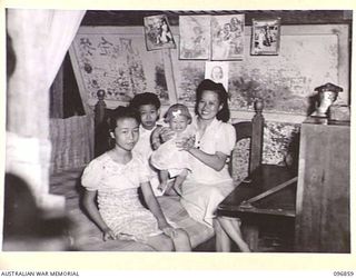 RATONGOR, NEW BRITAIN. 1945-09-13. THE PING FAMILY IN A TIN HUMPY, THE HOME THEY OCCUPIED FOR 22 MONTHS IN THE CHINESE INTERNMENT CAMP. IT WAS JUST LARGE ENOUGH TO HOLD A DOUBLE BED AND A WRITING ..