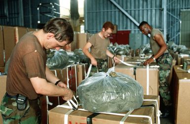 SSGT Thomas Johnson, foreground, 8th Mobile Aerial Port Squadron, rigs a parachute to a Christmas Drop container. The annual airdrop is a humanitarian effort providing aid to needy islanders throughout Micronesia during the holiday season