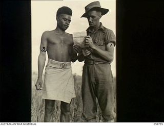 DUMPU, NEW GUINEA, 1943-10-10. QX40329 SERGEANT K.G. GUY OF HEADQUARTERS, 21ST AUSTRALIAN INFANTRY BRIGADE AND CORPORAL RAKA OF THE PAPUAN INFANTRY BATTALION, SHARE A HYMN SHEET, AT A CHURCH PARADE ..