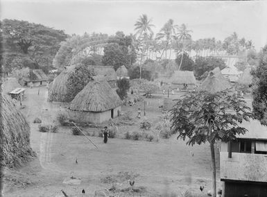 [High-angle view of a Pacific island village showing people and thatched dwellings]