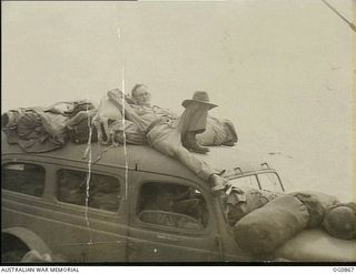 AT SEA BETWEEN GOODENOUGH ISLAND AND THE TROBRIAND ISLANDS, PAPUA. 1943-11-27. CORPORAL C. W. HARRISS OF HOBART, TAS, MAKES HIMSELF COMFORTABLE ON TOP OF A TRUCK TRANSPORTED AS DECK CARGO WITH NO. ..