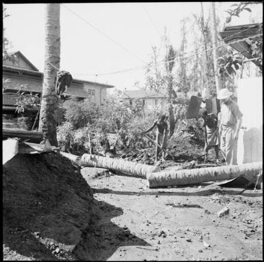 Man in a pith helmet and two men with shovels clearing debris amongst buildings, Rabaul, New Guinea, 1937 / Sarah Chinnery