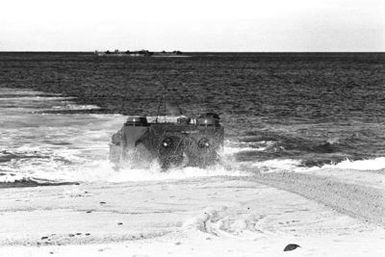 Marines come ashore on Makua Valley Beach in a tracked landing vehicle, personnel (LVTP 7) during Operation KERNEL BLITZ. The LVTP 7 is assigned to 3rd Amphibious Assault Battalion, 1ST Marine Brigade. In the background is an LCU 1610 class utility landing craft (LCU 1617)