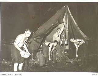 JACQUINOT BAY, NEW BRITAIN. 1944-12-17. MEMBERS OF THE MILITARY HISTORY SECTION FIELD TEAM ATTACHED, HEADQUARTERS, 5TH DIVISION, AND AN AMERICAN FRIEND REPAIRING DAMAGE CAUSED BY A HEAVY TROPICAL ..